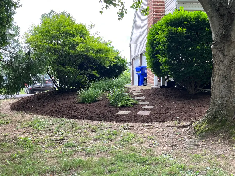 Mulched bed with stepping stones and shrubs beside a house, by Hilltop Lawn Care LLC