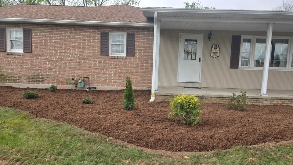Fresh mulch beds and new plantings along the front of a brick house, by Hilltop Lawn Care LLC